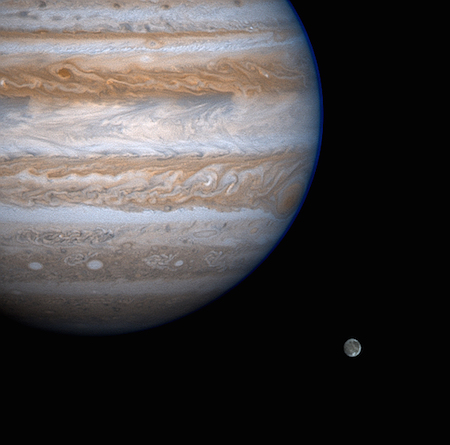 Một bức ảnh chụp Sao Mộc ở góc trên cùng bên trái, cho thấy rõ các dải màu của Sao Mộc: nâu, xám và đỏ. Một mặt trăng nhỏ ở góc dưới bên phải.